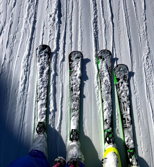 Es sind zwei paar Skier nebeneinander im Schnee zu sehen. Die Marken sind unter einer Schneeschicht bedeckt.